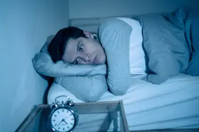 man awake in bed looking at his vintage alarm clock