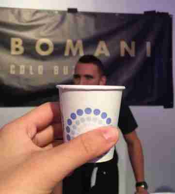 Holding up a paper cup in front of the CEO of Bomani cold buzz. One of the booths in the New York City Coffee Festival. 