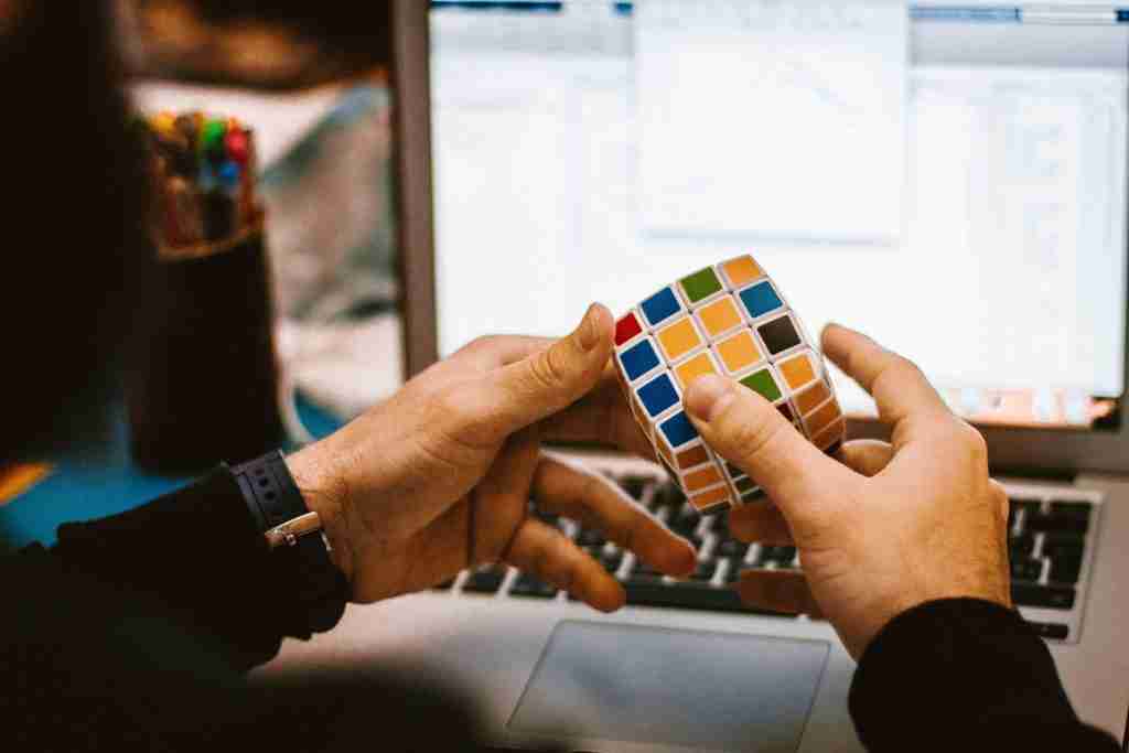 hands playing with a Rubiks cube in front of a work laptop